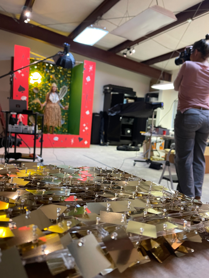 A photographer captures a model inside an elaborate set piece, with a glittering sculpture in the foreground.