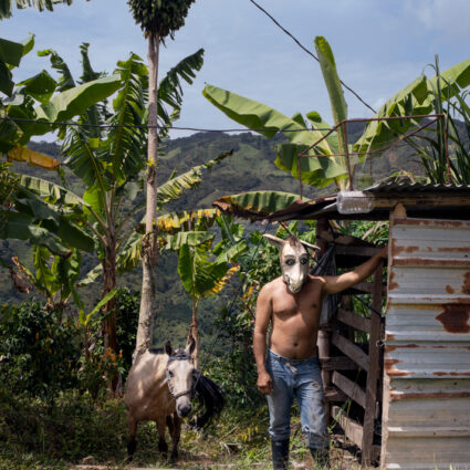 Photographic portrait showing a man in a donkey mask. A donkey stands behind him. Curated by Maria Elena Ortiz.