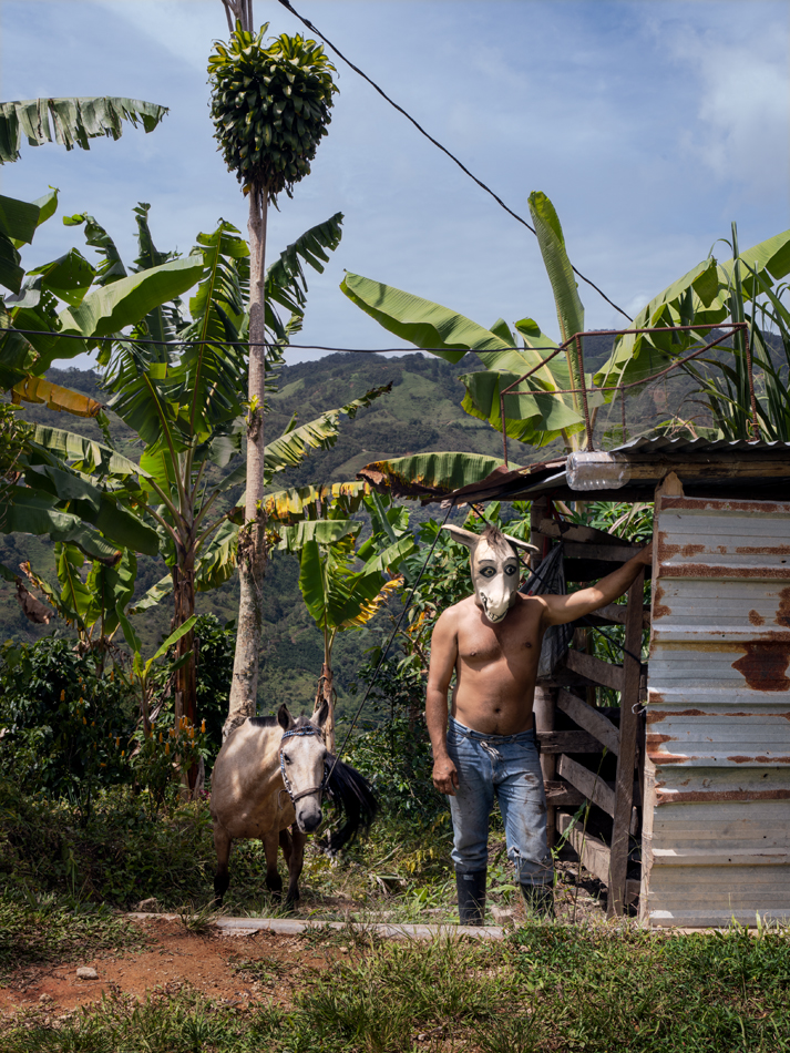 Photographic portrait showing a man in a donkey mask. A donkey stands behind him. Curated by Maria Elena Ortiz.