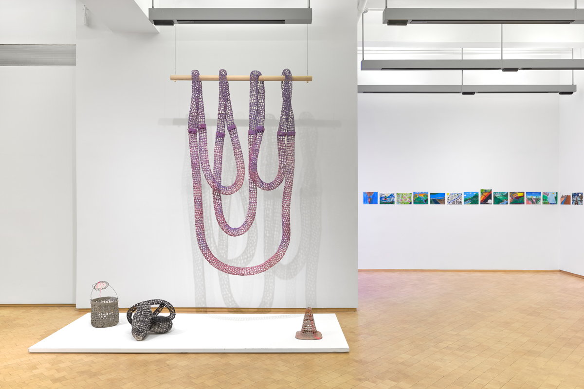 Artworks in a contemporary museum space, including a suspended installation in a purple ombre palette. Curated by Maria Elena Ortiz.