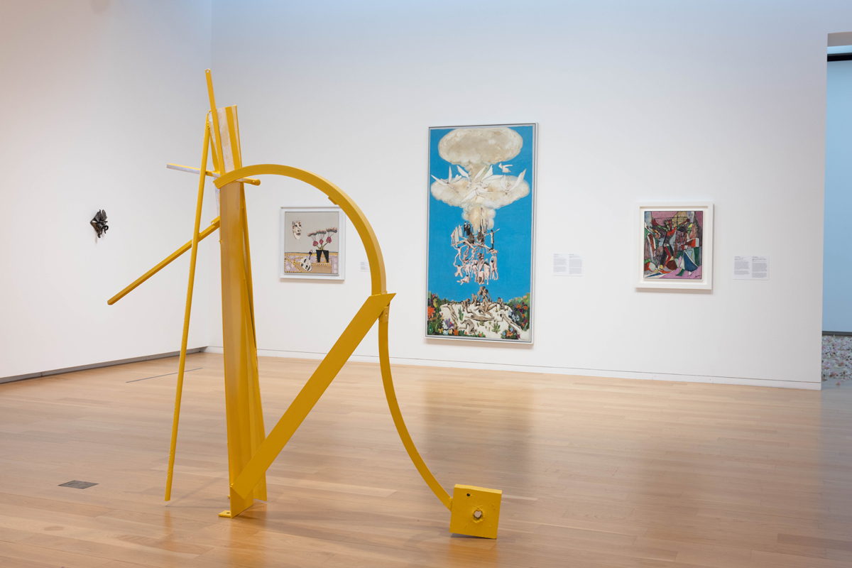 Installation view of a museum show featuring a yellow abstract sculpture and multiple wall pieces. Curated by Maria Elena Ortiz.