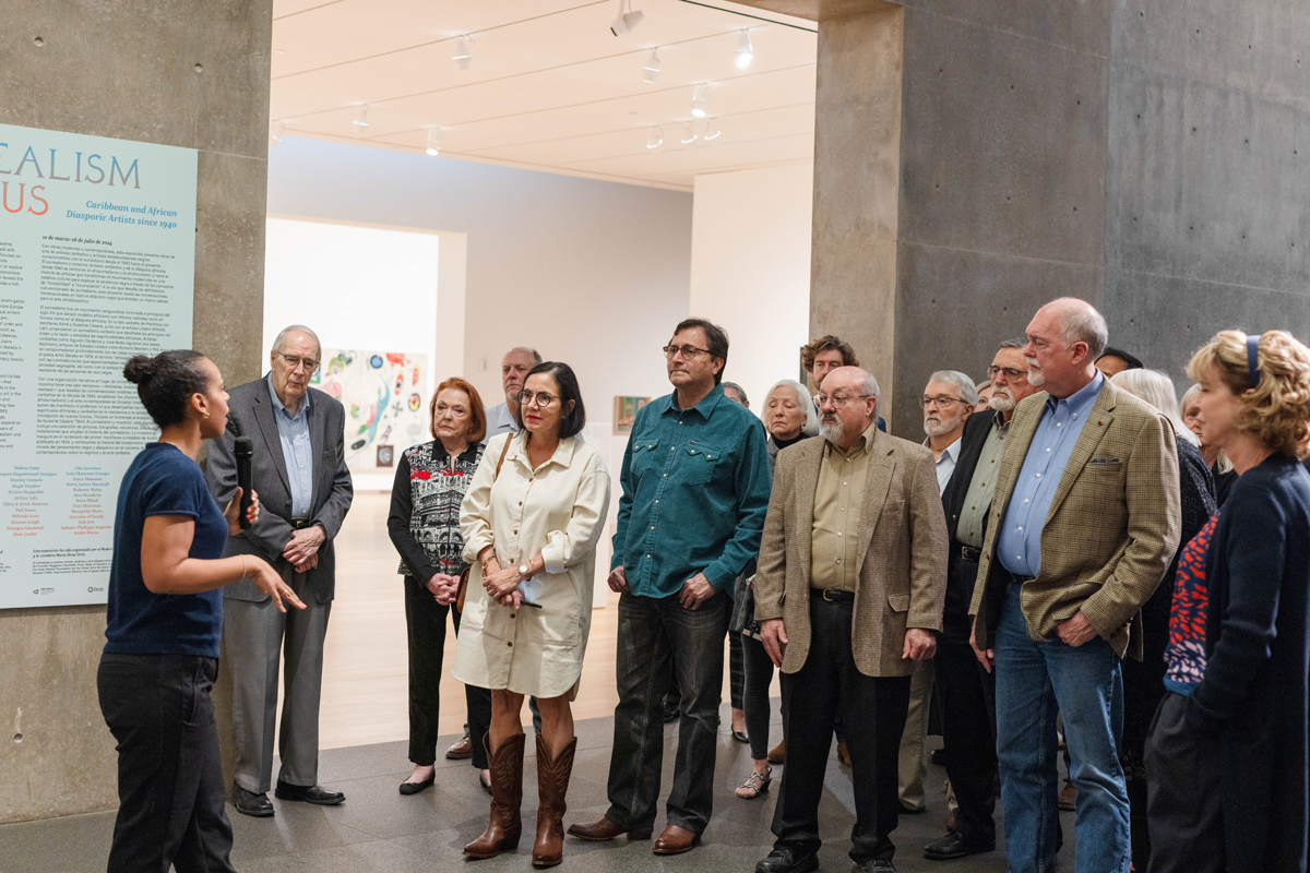 Curator María Elena Ortiz speaks to a crowd in a contemporary museum space.