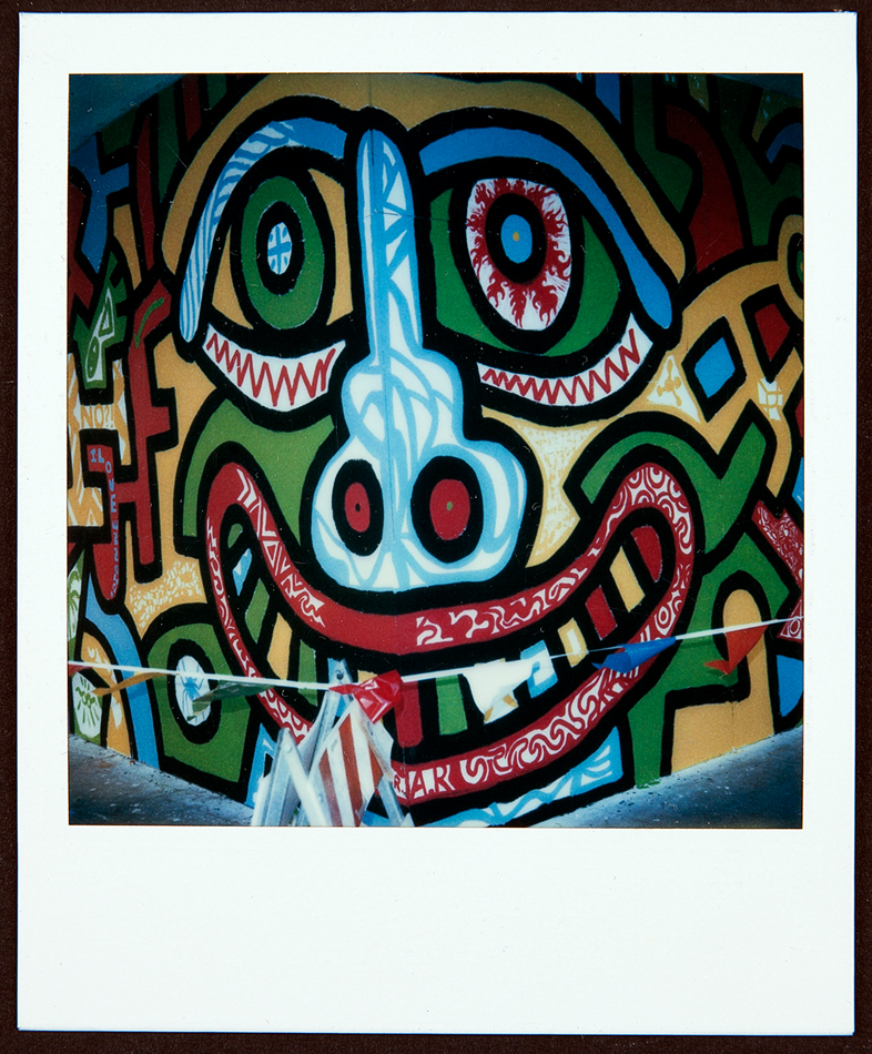 Polaroid of a mural depicting a smiling face, with line work by Keith Haring and coloring by Phoenix high school students.