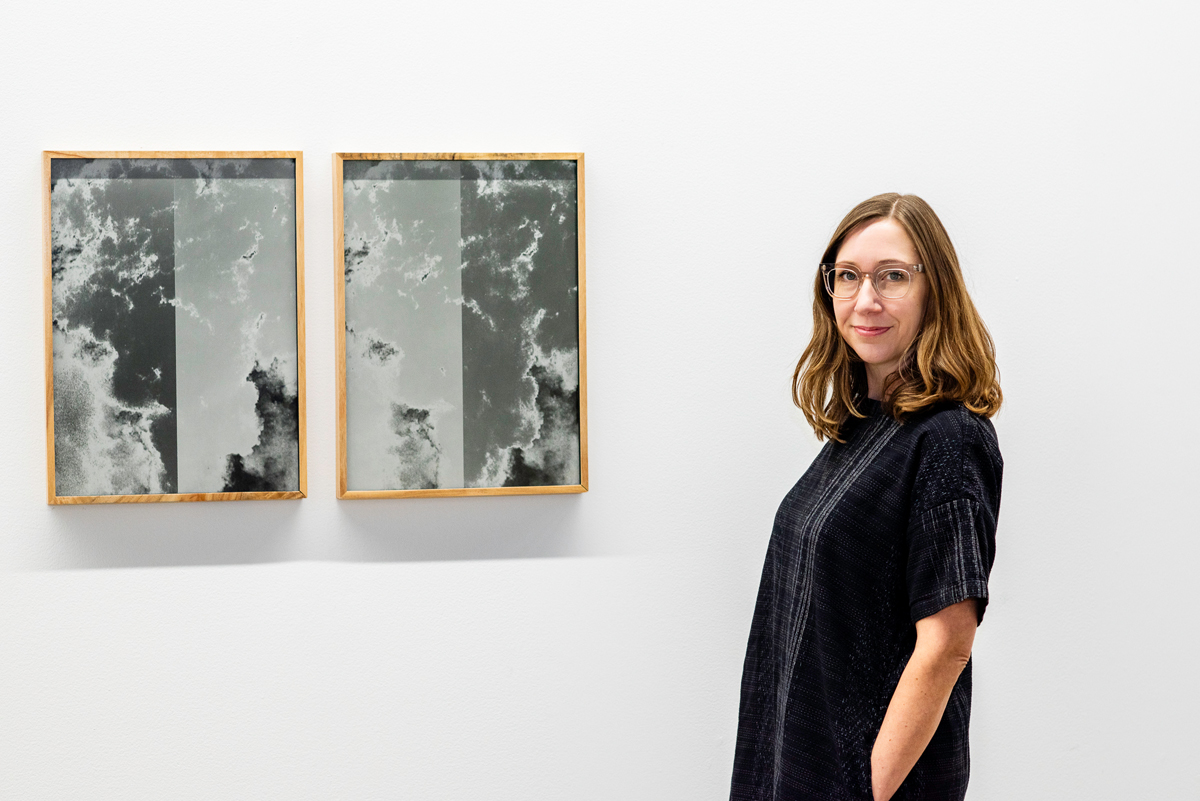 A woman dressed in black stands beside two framed, grayscale artworks. Looking back on curatorial path of the Kimball Art Center's Nancy Stoaks.