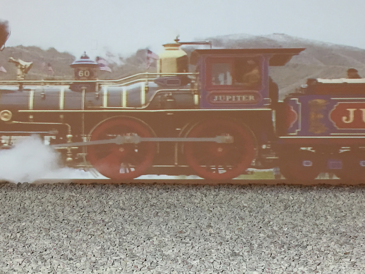 Still of a video projection showing a locomotive steam engine. Below it, a field of loose stones completes the art installation.