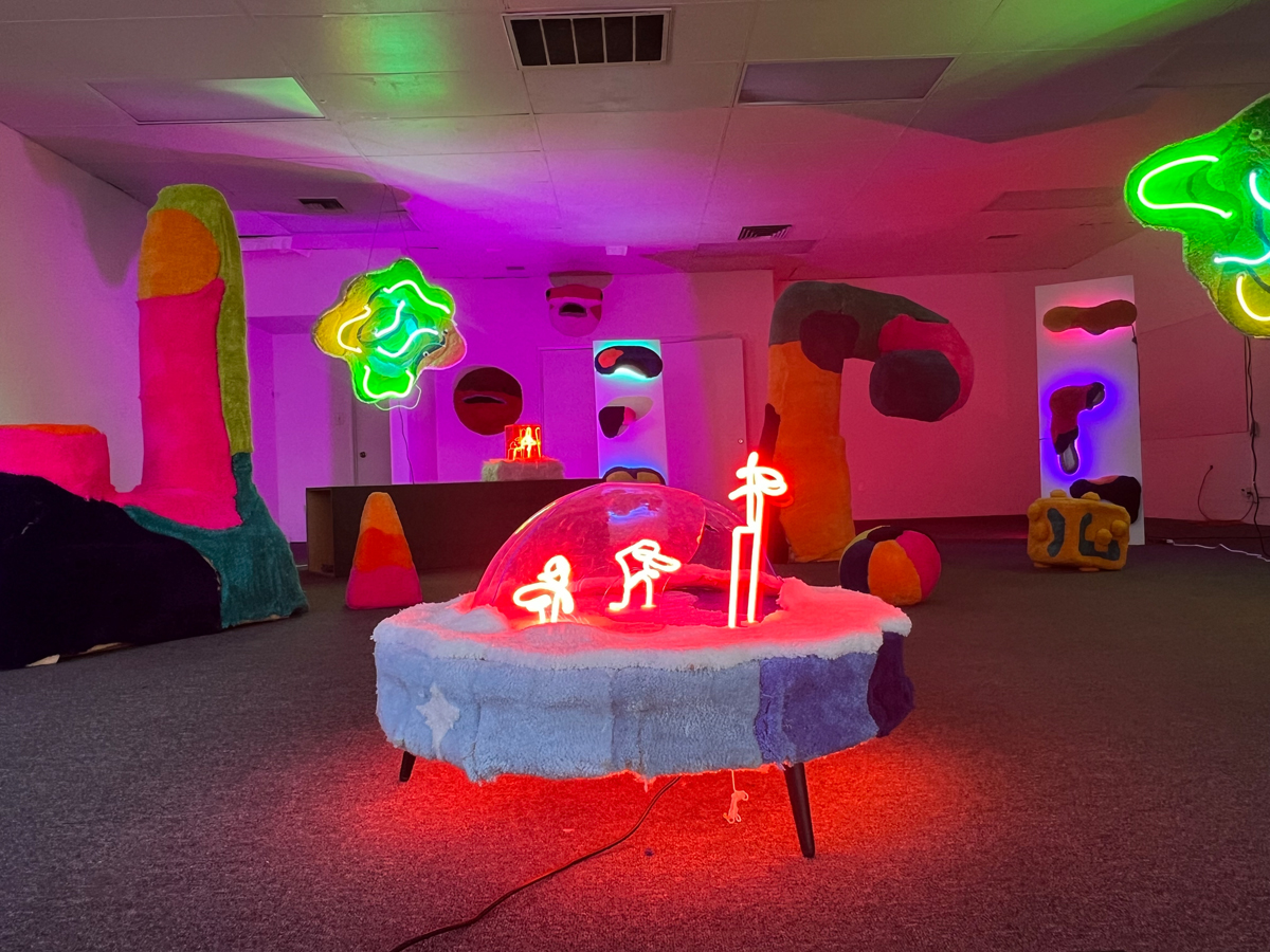 An art installation featuring fuzzy sculptural forms and glowing neon in red and green. Alternative arts hub Danelle Plaza in Tempe, Arizona, faces uncertainty amid redevelopment plans.