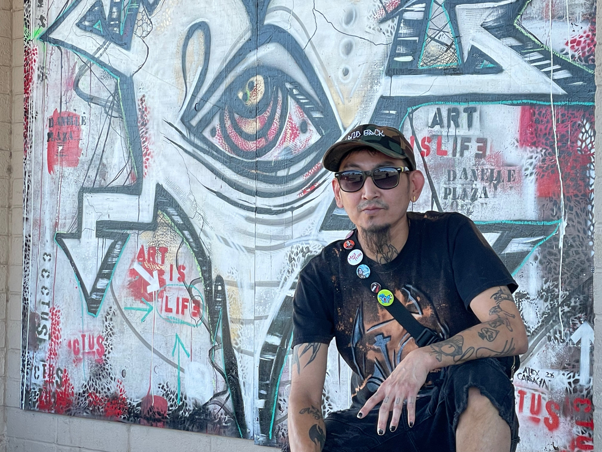 A man in a baseball cap kneels before a mural with an eye motif. Alternative arts hub Danelle Plaza in Tempe, Arizona, faces uncertainty amid redevelopment plans.