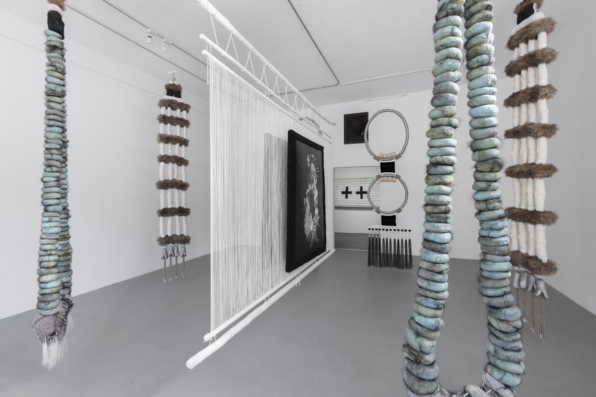 Suspended fiber installation with strands of soft sculptures that evoke beads.