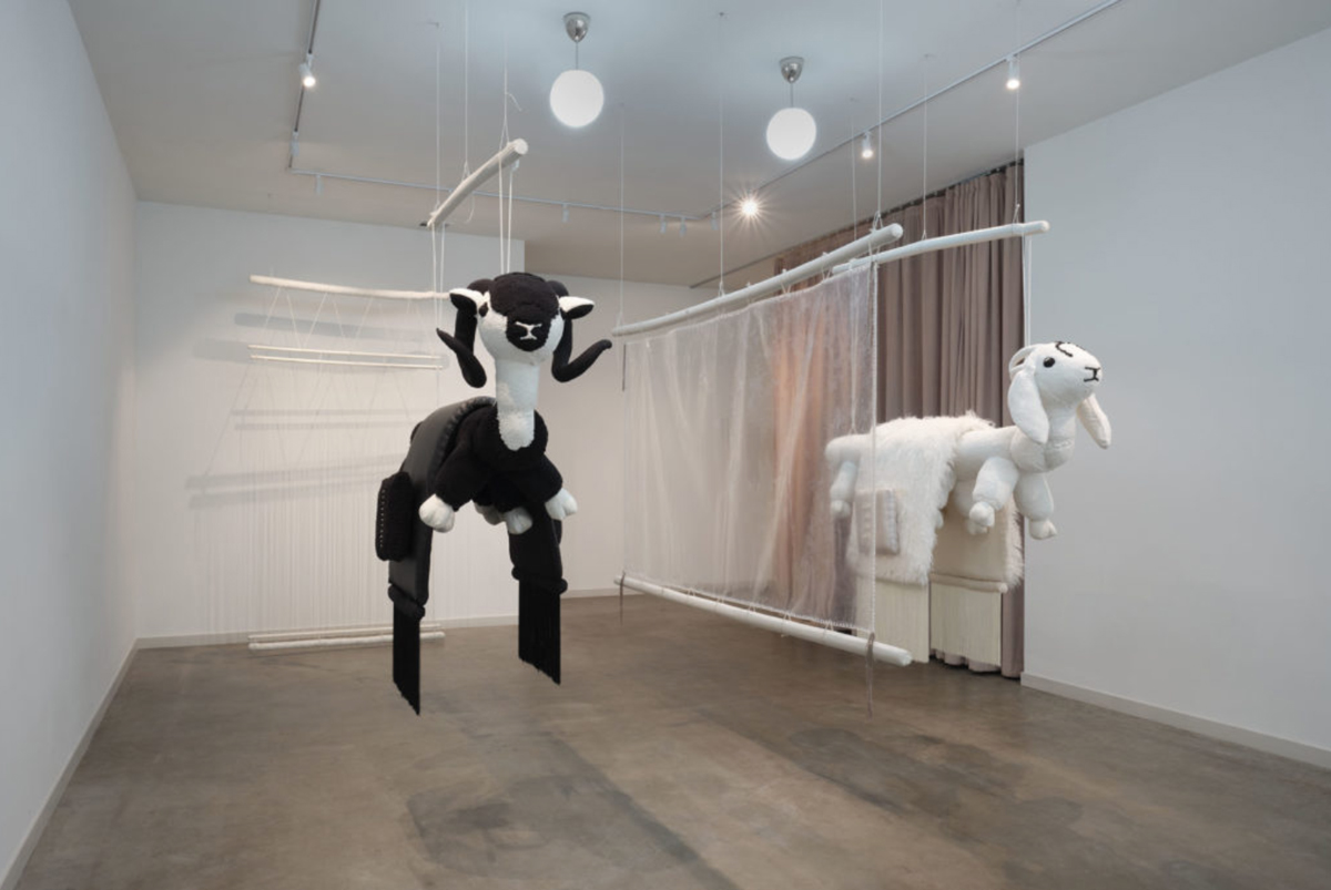 A suspended fiber installation featuring mixed-media sheep forms and translucent veils by Eric-Paul Riege.