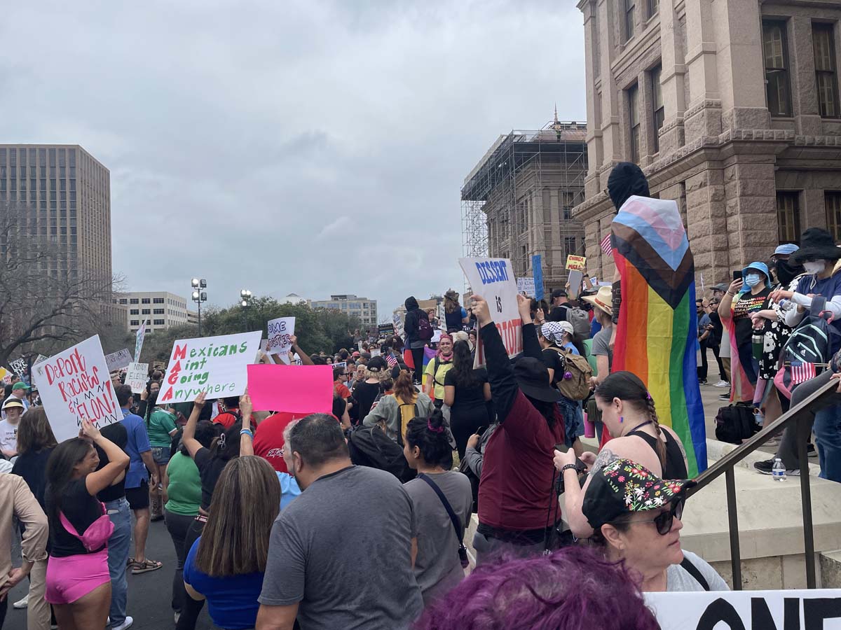 Protest outside of the Texas State Capitol, with one protester draped in a BIPOC rainbow flag.