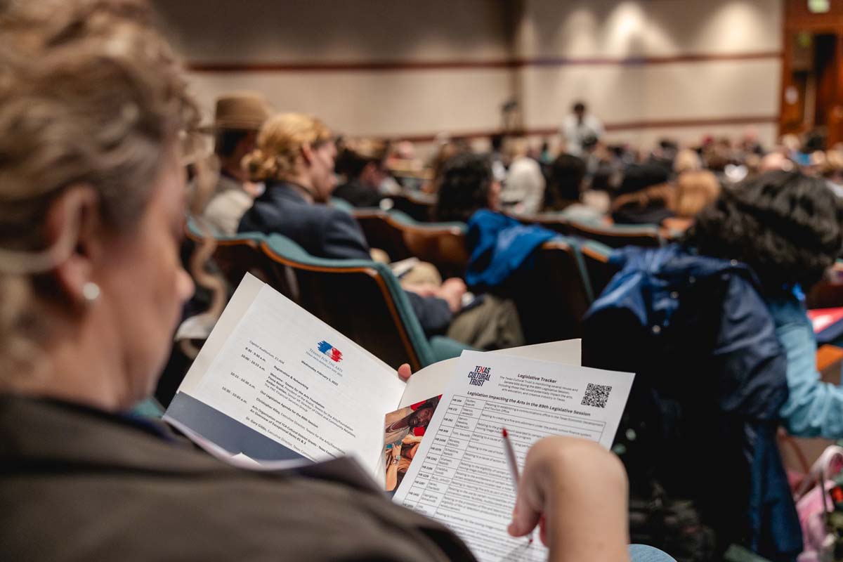 Attendee of Texas Arts Advocacy Day looking at a folder of information while sitting in the Capitol Auditorium.