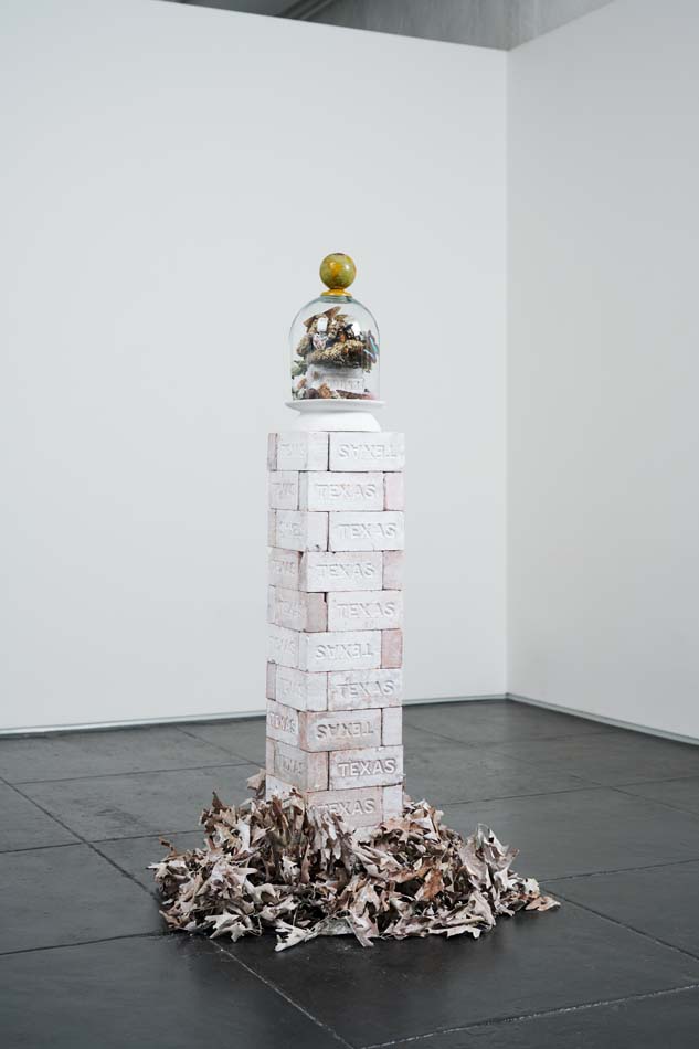 Interdependence, by Cindee Klement, a column of Texas-stamped bricks holding up a deli- cate bell jar containing a still-life composition of shells, butterflies, a bird nest, and other natural elements.