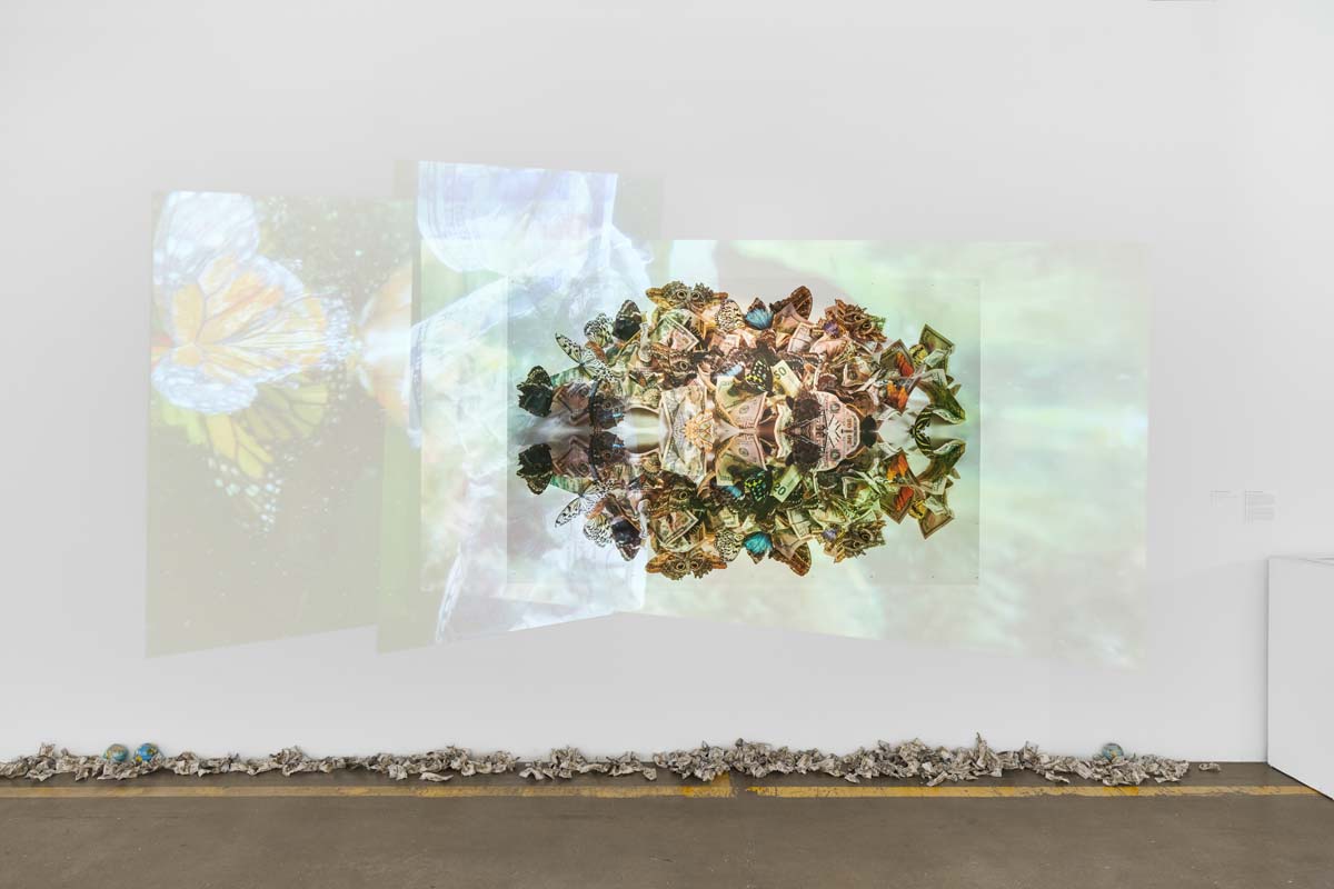 An installation with projected video, print and a line of crumpled dollar bills on the floor below it.