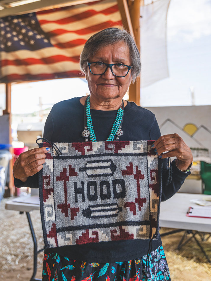 Portrait of a woman holding a weaving that says "Hood." Photo by Shayla Blatchford for Anti-Uranium Mapping Project.