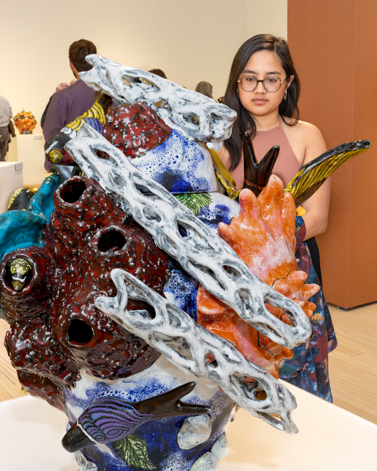A woman looks at an intricate ceramic artwork by Farraday Newsome.