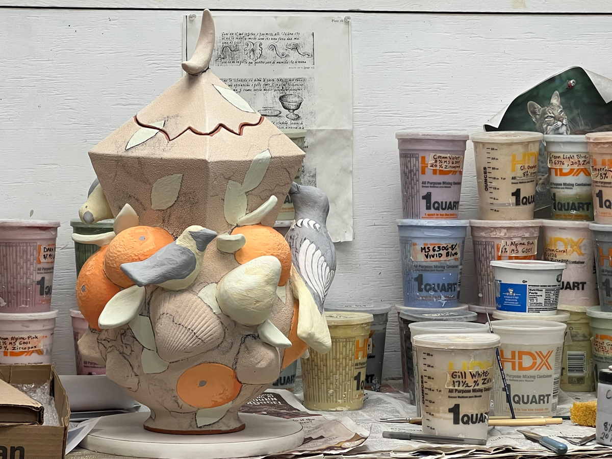 An in-progress ceramic artwork with tubs of glaze behind it.
