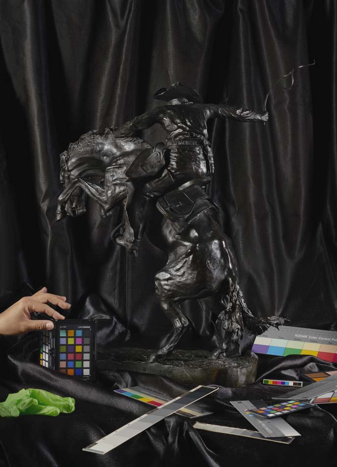 Photograph by Stephanie Syjuco depicting a Fredric Remington bronze cowboy against a black background.