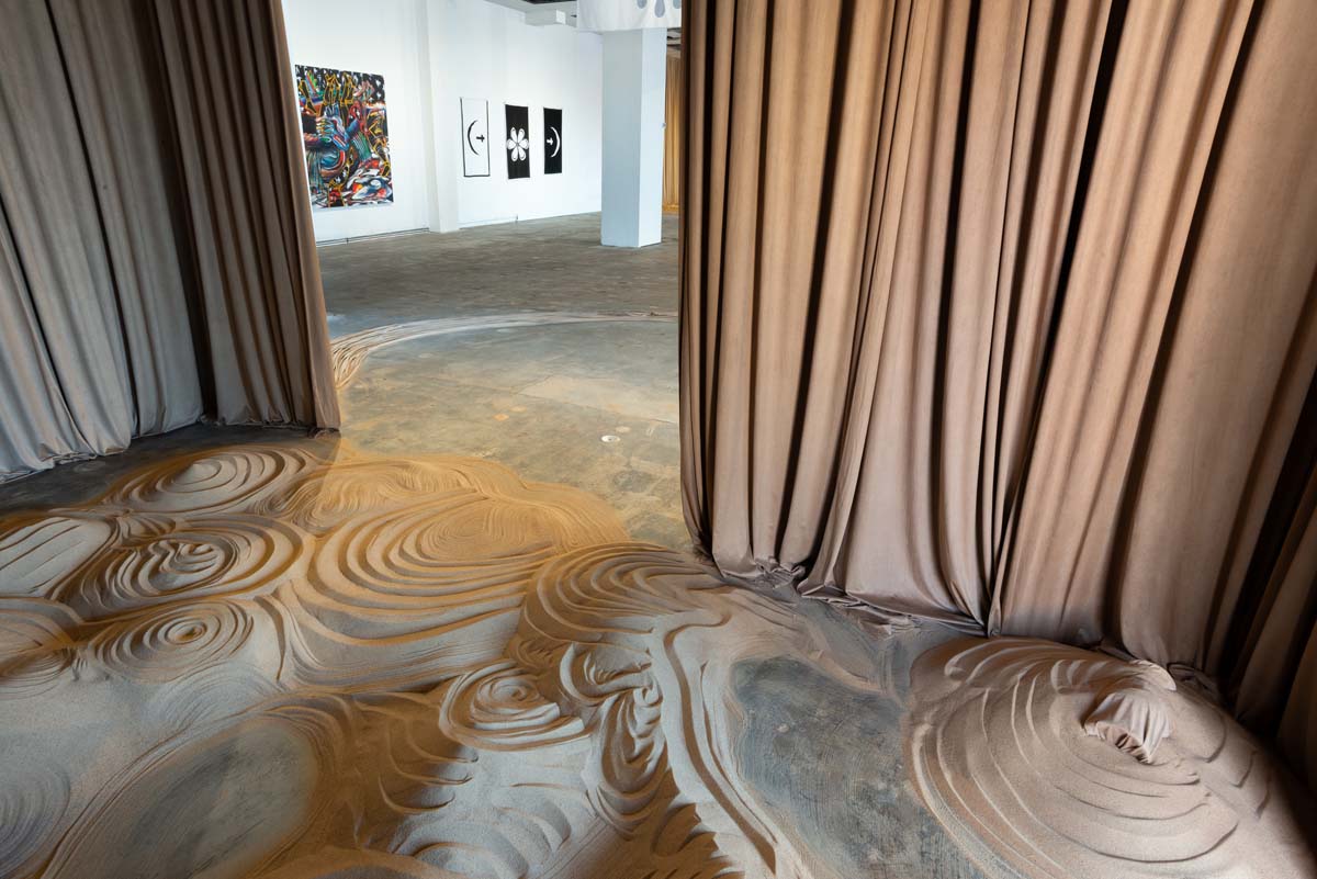 A cascade of earthen-hued fabric spilling ceiling-to-floor into sand