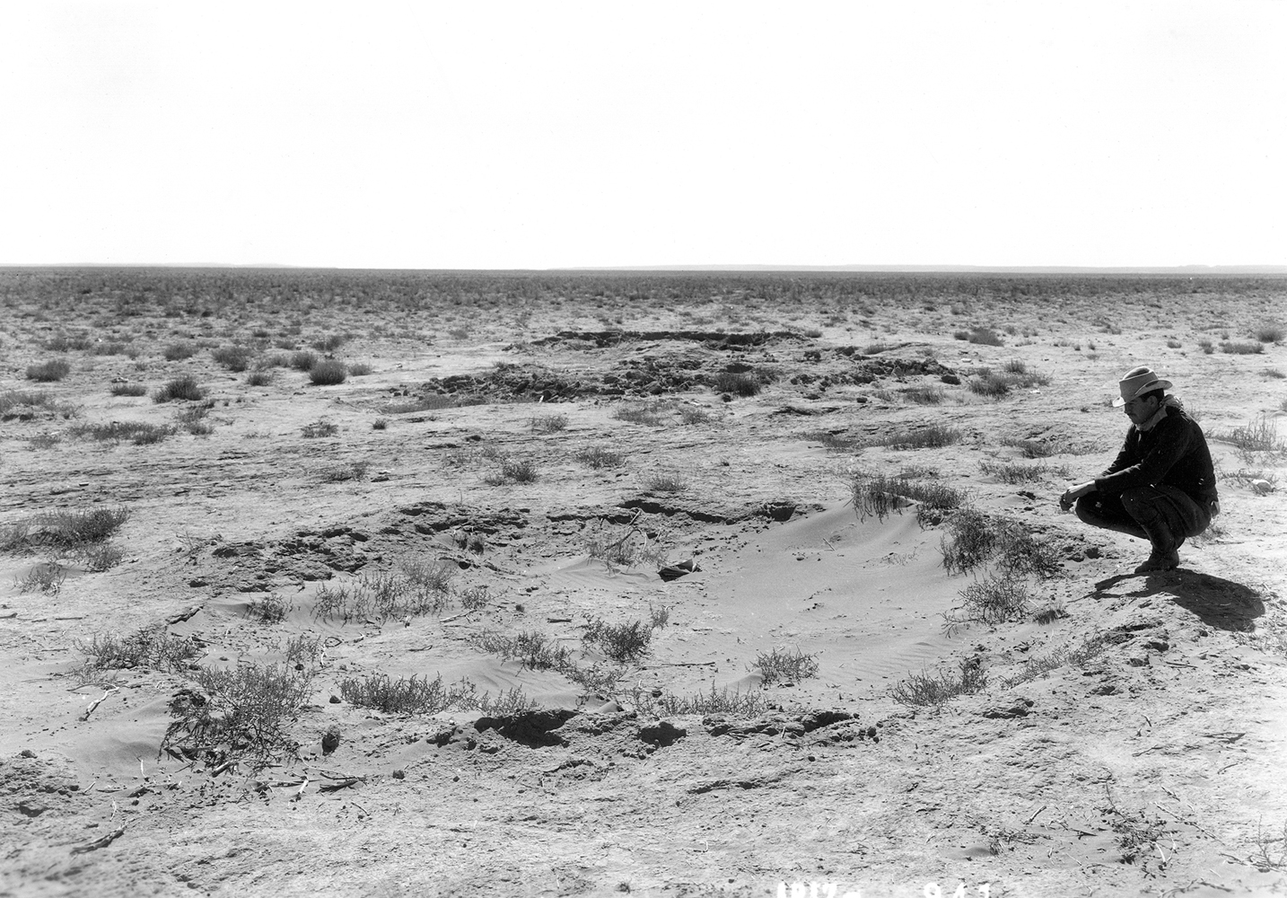 Historical photograph by Milton Snow of a man crouching in an expanse of Southwestern desert. Maxwell Museum of Anthropology in Albuquerque is working with the Navajo Nation Museum to fill in the gaps outside the frame.