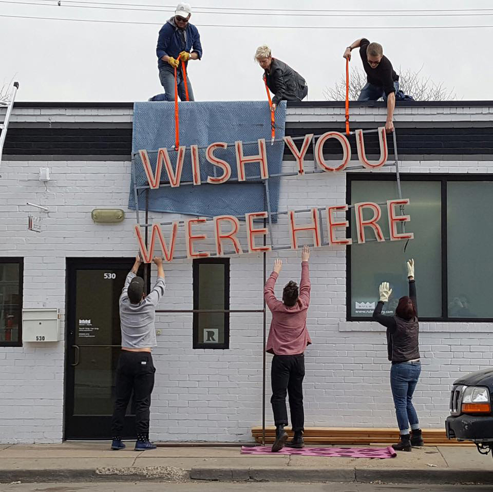 Artists and gallery workers de-install a sign that reads Wish You Were Here at Rule Gallery Denver.