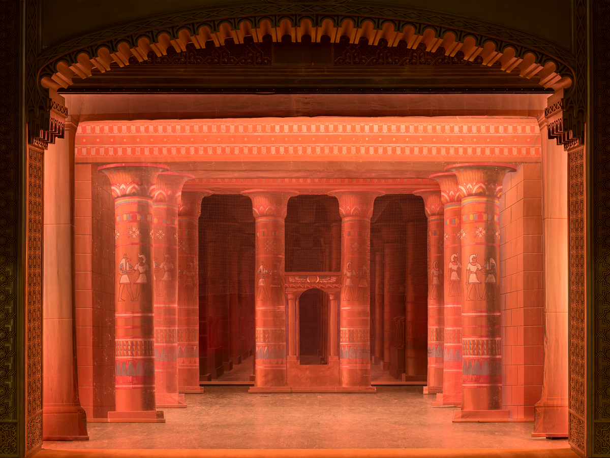A red stage set depicting a temple interior, including pillars with elaborate designs on them.