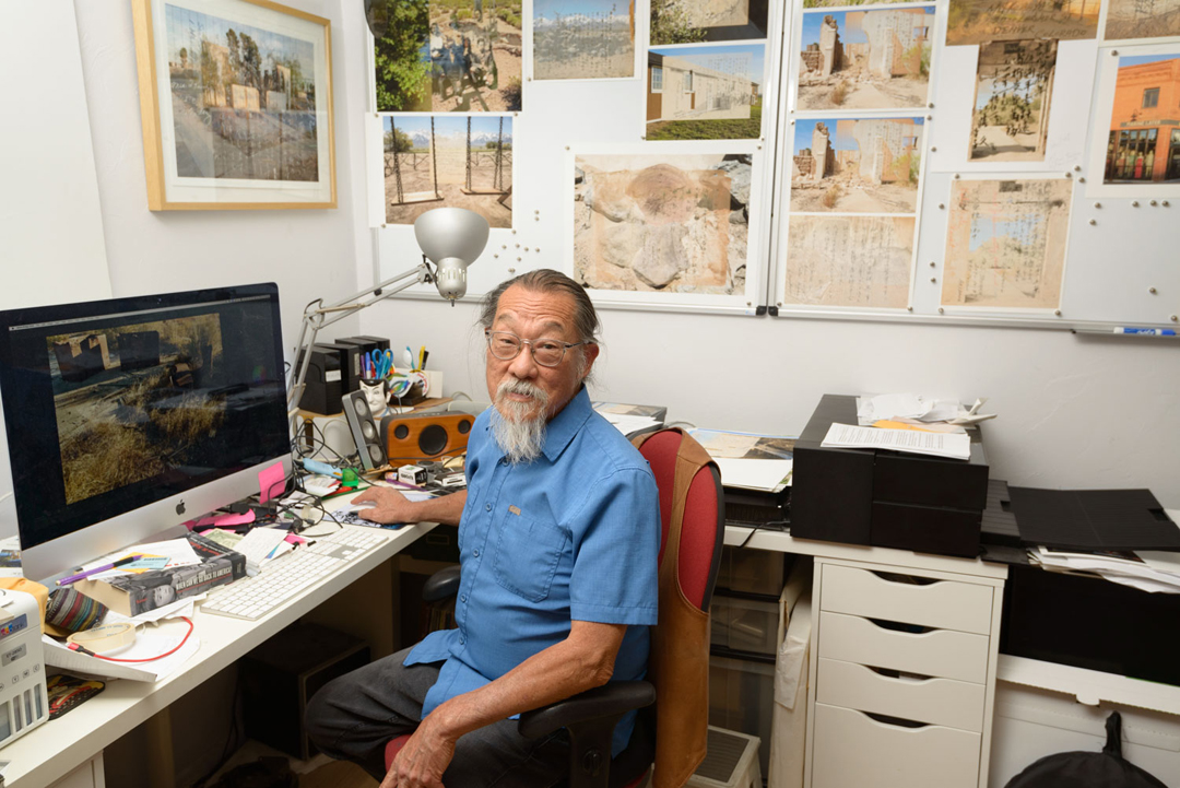 Phoenix artist Dean Terasaki sits at his computer monitor, with artwork proofs pinned to the wall behind him.