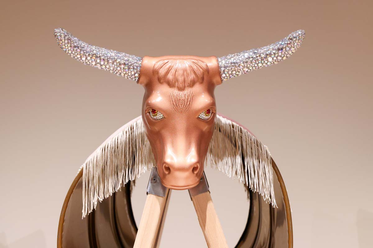 A rose gold bull head with diamond encrusted horns attached to a fringed barrel and saw horse.