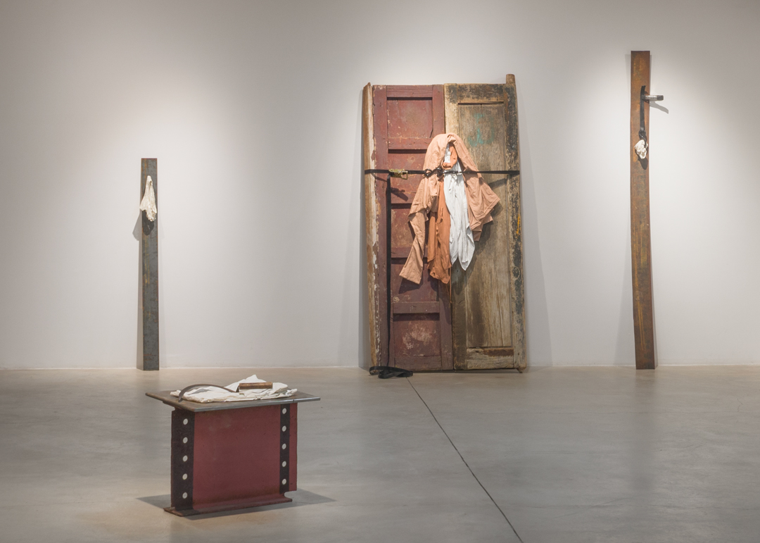 Installation view of an exhbiition by Daisy Quezada Urena featuring architectural elements including a door and fence pieces. The Santa Fe-based artist will participate in the SITE Santa Fe International, Once Within a Time.