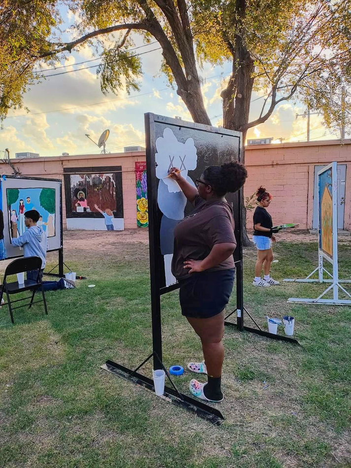 People paint murals on panels during a pop-up art event by Danielle Demetria East, a project that directly addresses the Texas Housing Crisis.