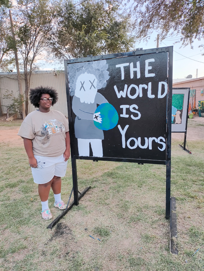 An artist stands beside a mural reading "The World is Yours."