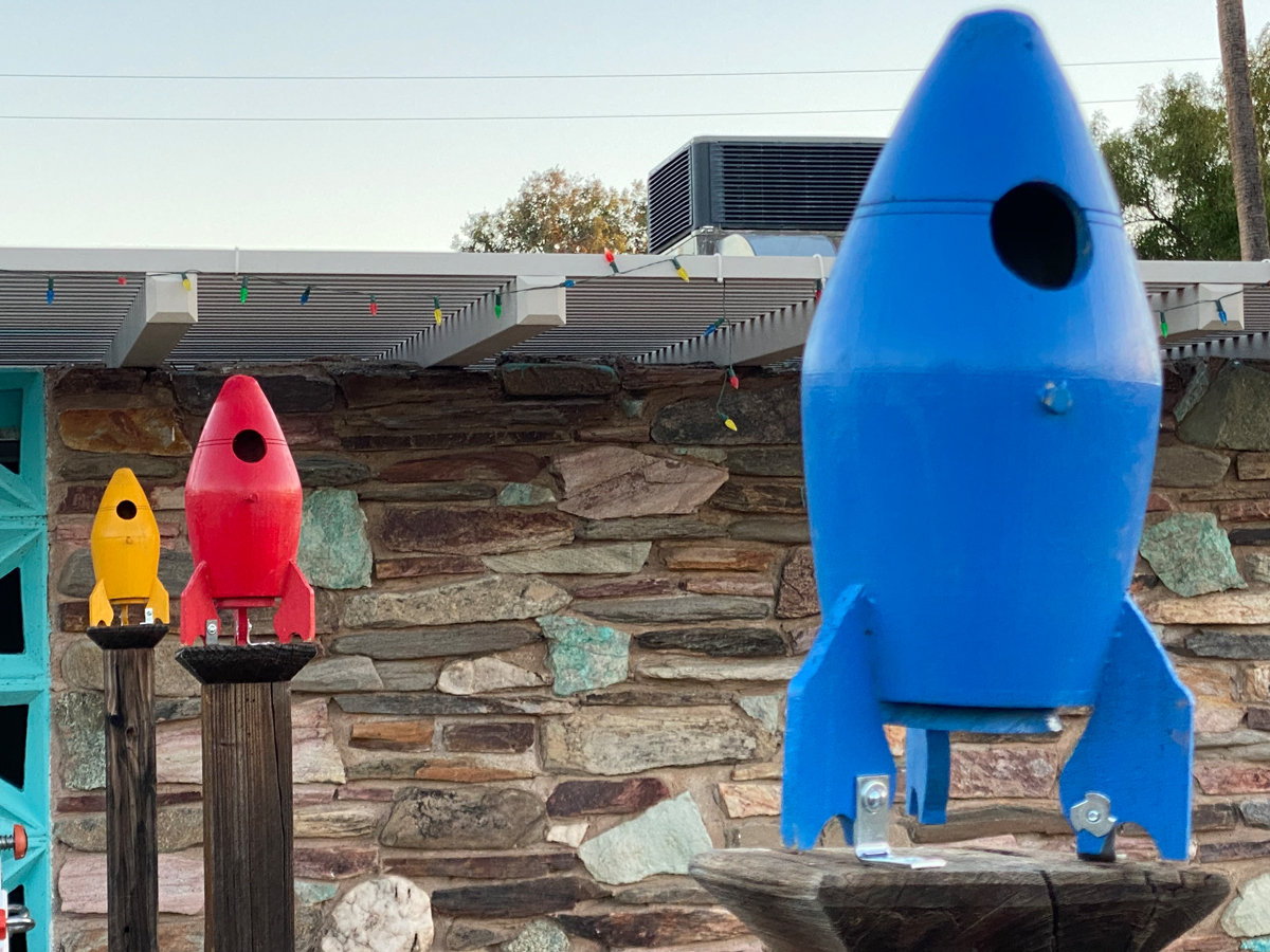 Three rocket ship birdhouses in blue, red, and yellow.