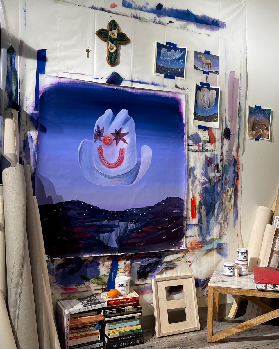 View of an art studio maintained by Grace Kennison in Ridgway, Colorado, with a painting of a smiley-face cowboy hat floating above a dusky landscape.