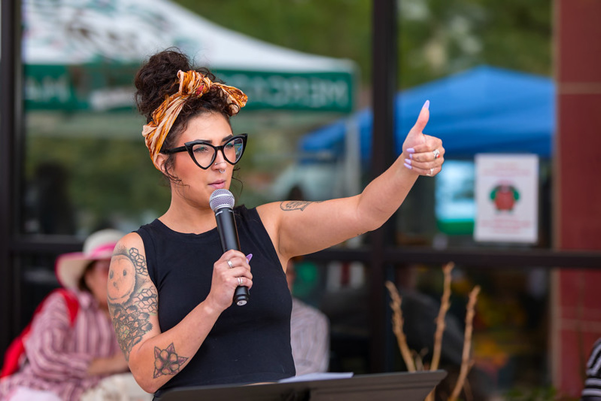 A woman holds a microphone and flashes a thumbs up. The Athena Project is just one of the many Southwest arts organizations facing NEA funding cuts.