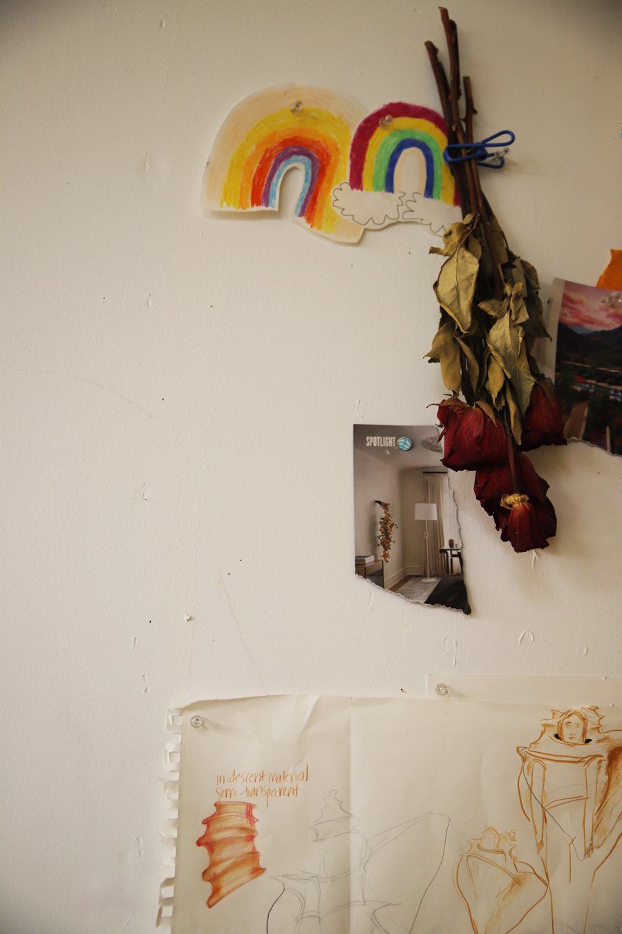 The wall of an artist studio, with rainbows, drawings, and flowers tacked around.