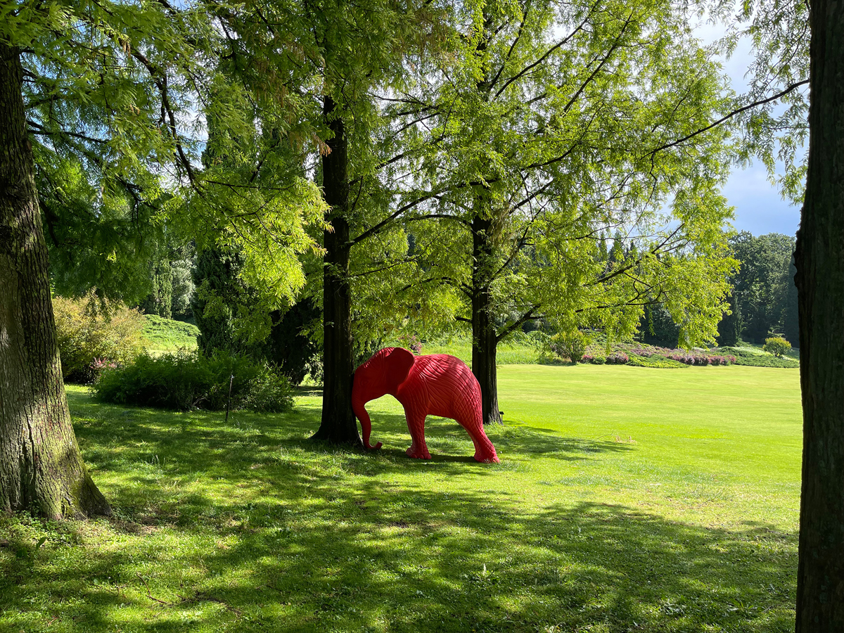 A sculpture of a red elephant leaning against a tree.