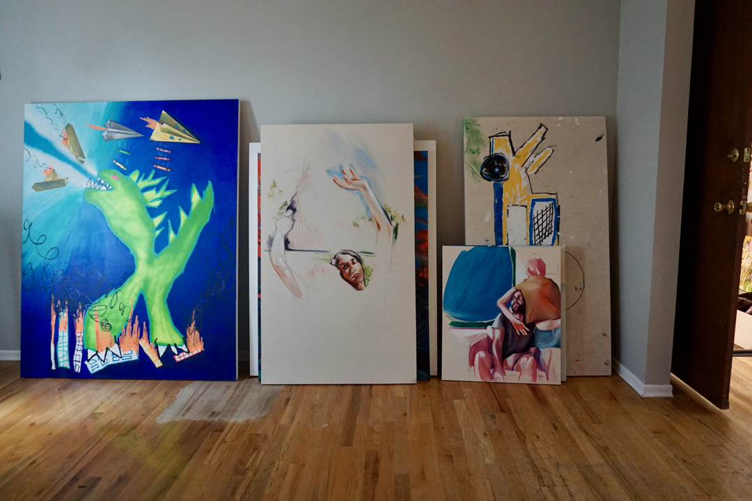 Paintings by Kaitlyn Tucek and Matt Tripodi, two Denver-based artists, stacked against a studio wall.