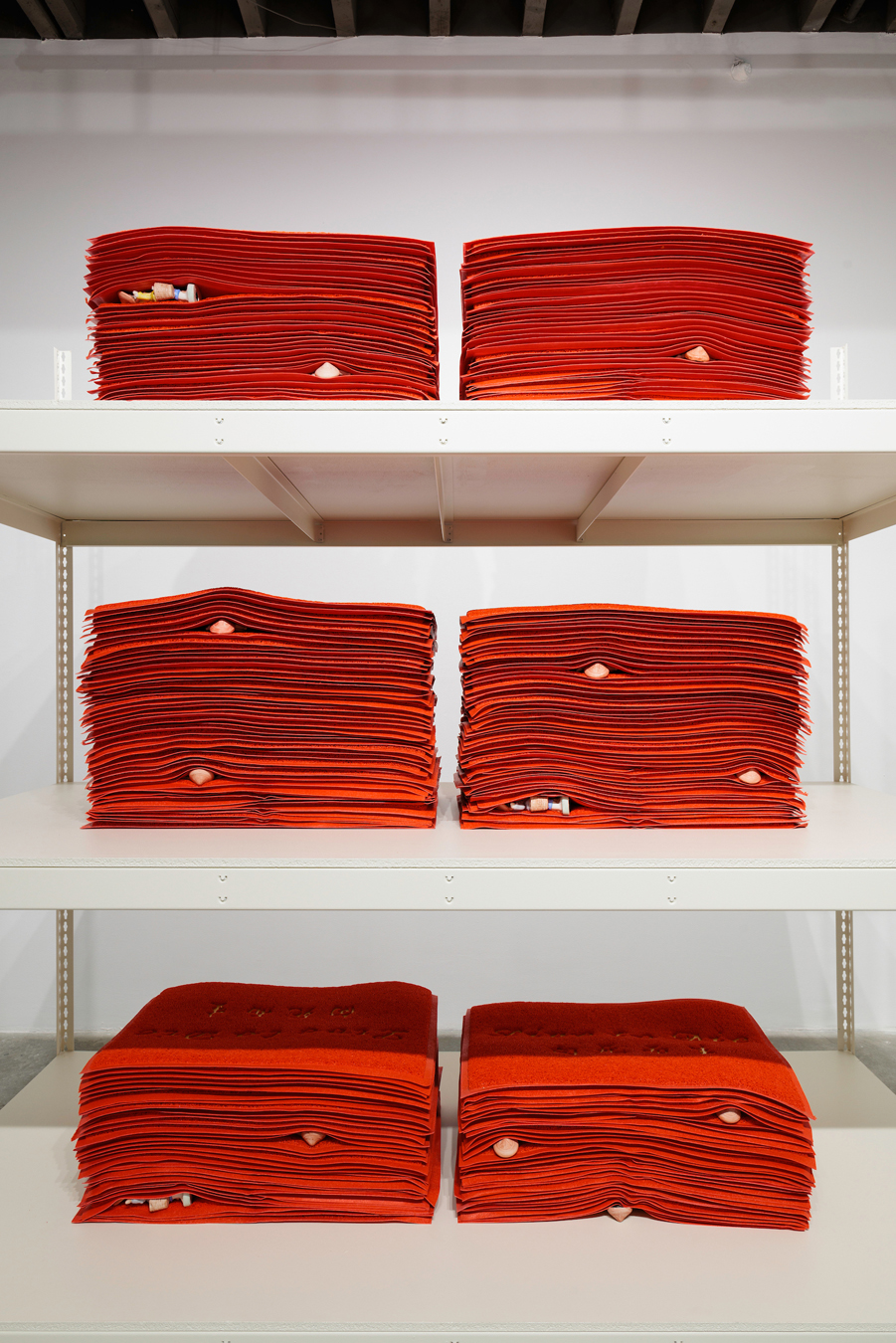 Large-scale installation featuring stacked red welcome mats with porcelain wedged between them.