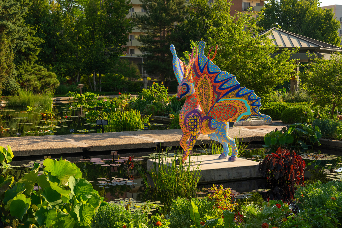 Winged creature referencing the Oaxacan alebrije tradition in a verdant garden. Southwest Botanical Gardens have transformed into living contemporary art museums.