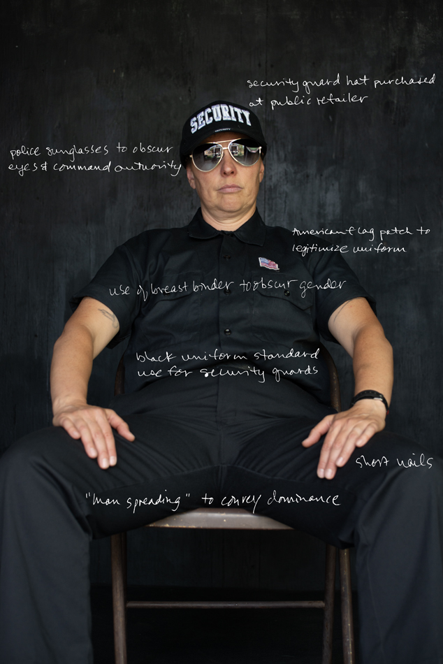 Photograph of artist jesse lovell in one of their disguises as a security guard. Artist sits in a chair facing the camera wearing a security guard uniform and aviator sunglasses.