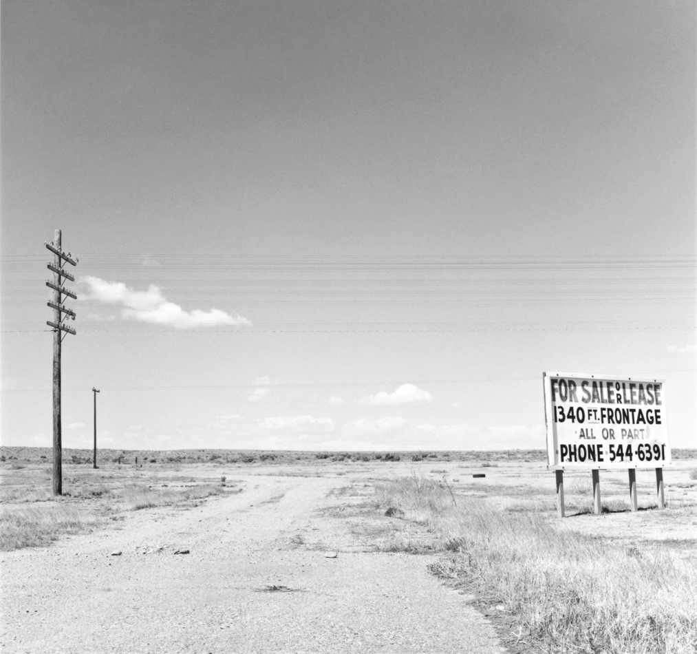 Black and white photo by Robert Adams showing a For Sale/Lease sign along Interstate 25.