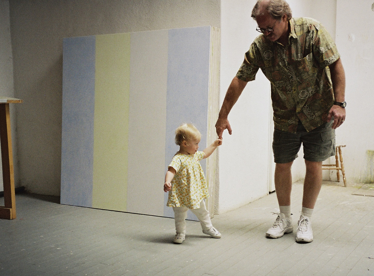 A baby and a man dance in front of an Agnes Martin painting in the artist's studio.