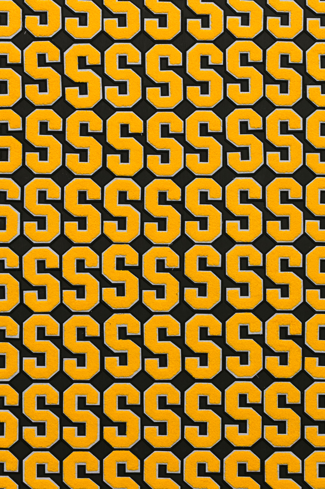 Close-up photo of Denver-based artist Joel Swanson's artwork titled "Crusaders", featuring the repetition of yellow chenille letter S on a wood panel painted dark navy blue.