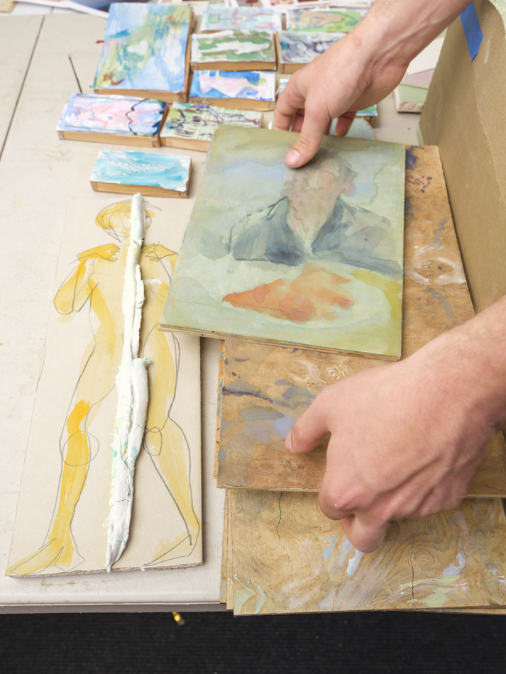 Eli Ruhala examines small-scale paintings in his studio.