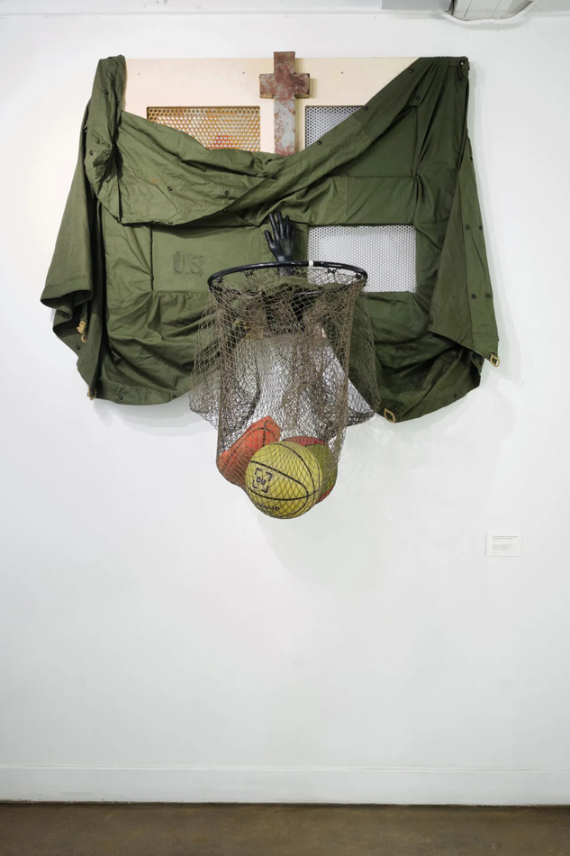 Found object sculpture forming a basketball hoop with multiple basketballs caught inside a hoop made of fish netting. By Phoenix-based artist Philip Gabriel Steverson.