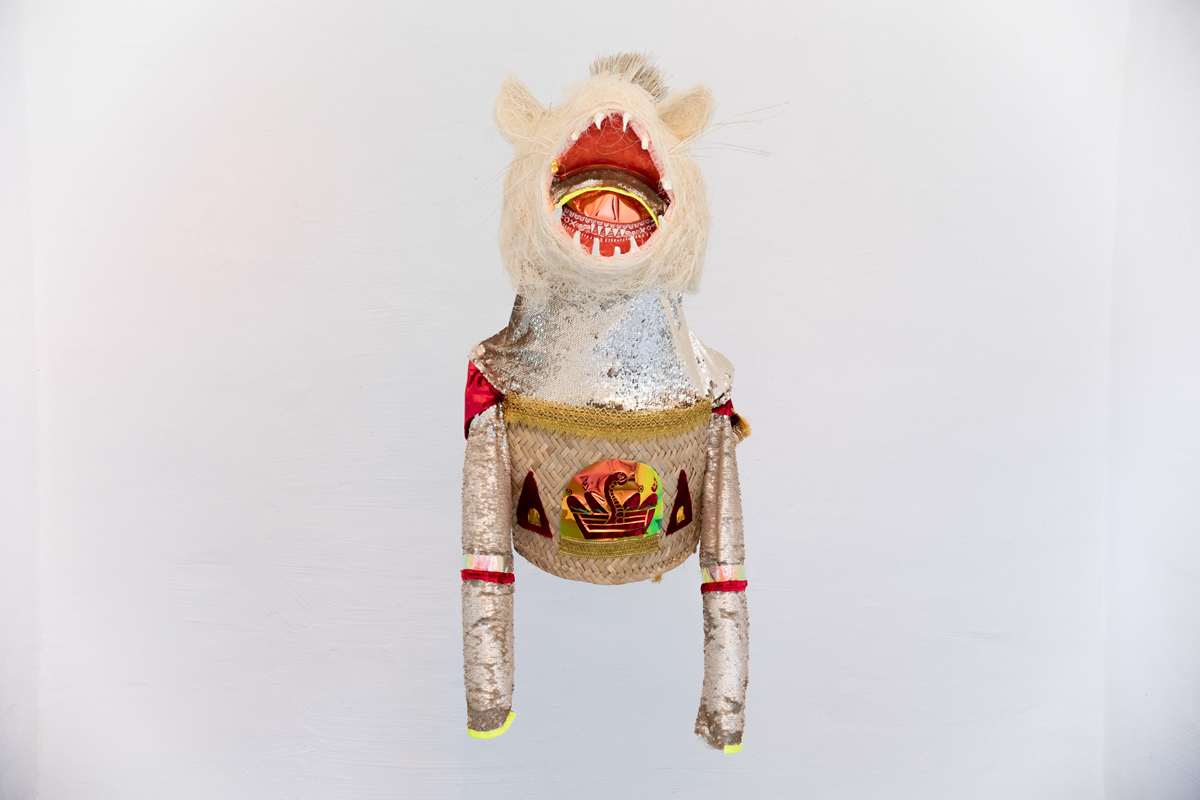 Photo of a wearable sculpture with a white animal head, basket-woven torso, and gold and silver sequins by artist Federico Cuatlacuatl. 