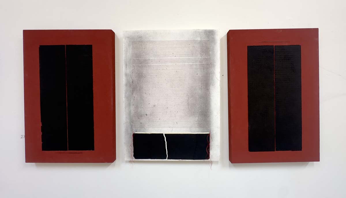 A triptych by Judy Tuwaletstiwa in glass, white thread on paper, in the center panel, with the two outer panels of glass, black in the center and framed in red.