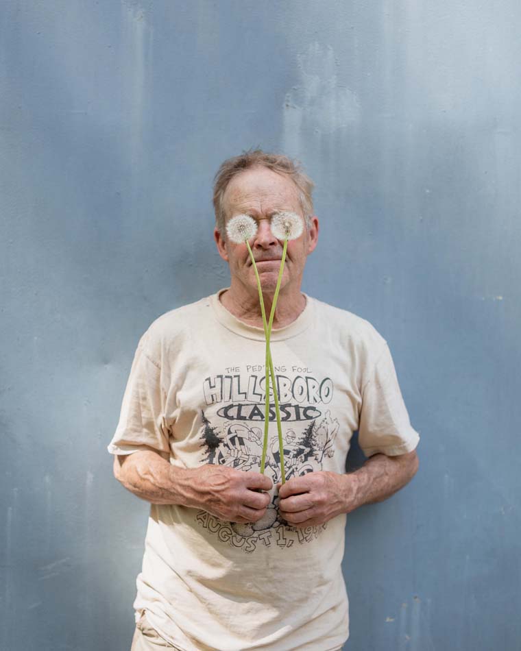 Man holding two long stemmed dandelions in front of his eyes.