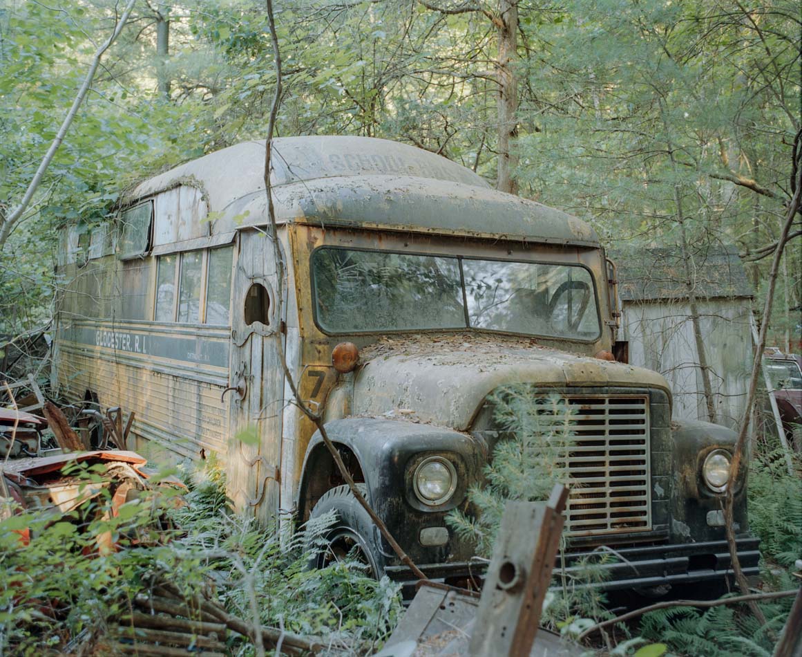 Photograph of an old abandoned bus in the an overgrown wooded area.