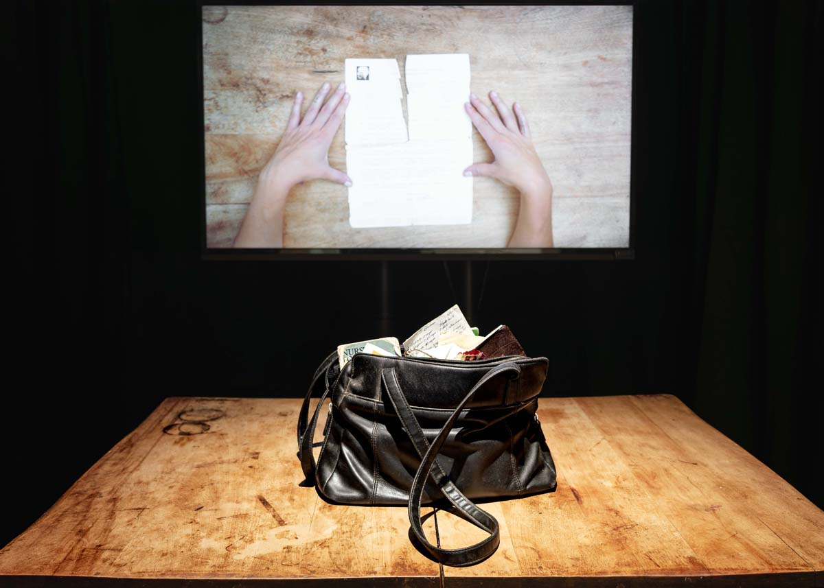 Video installation with a video projection behind an old leather handbag on a kitchen table.