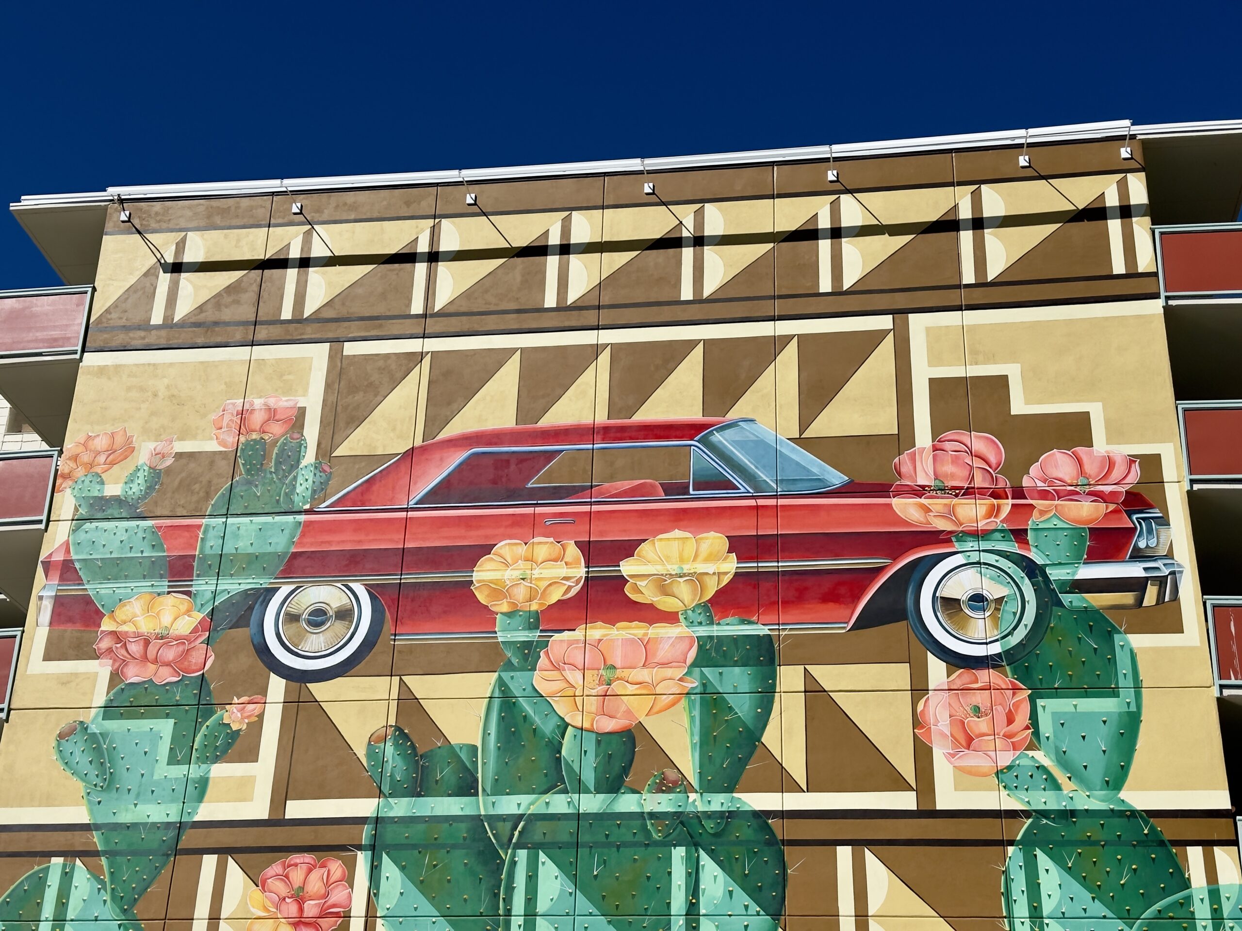 Mural by artist Nani Chacon featuring a red lowrider and flowers, part of the essential Southwest Mural Guide.